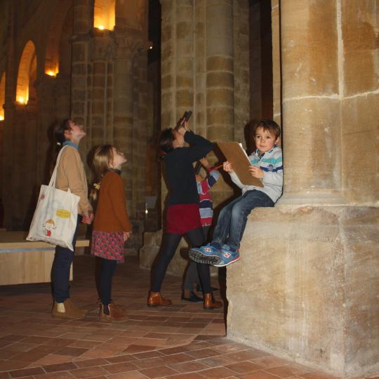 Un groupe d'enfant observent l'architecture des voûtes romanes de la nef de l'église.