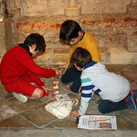 Trois enfants construisent une arche romane en bois sur un sol en pierre dans l'Abbaye de Graville.