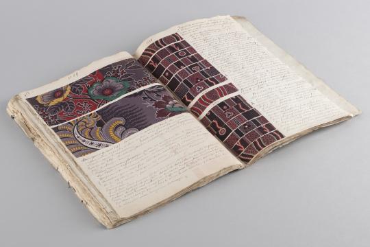 Cahier ouvert présentant des échantillons de tissus et du texte.