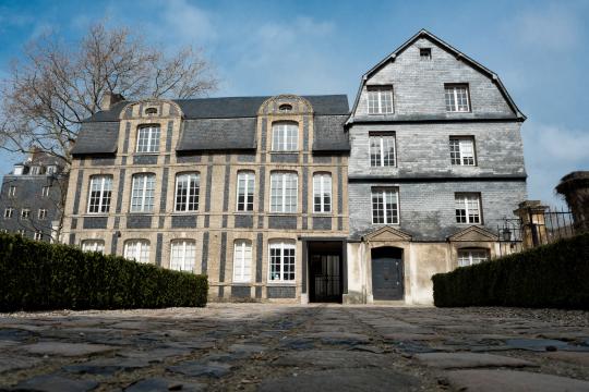 Vue extérieur du bâtiment. Les murs sont en briques jaunes et silex noirs. La partie droite est essentée d'ardoises.