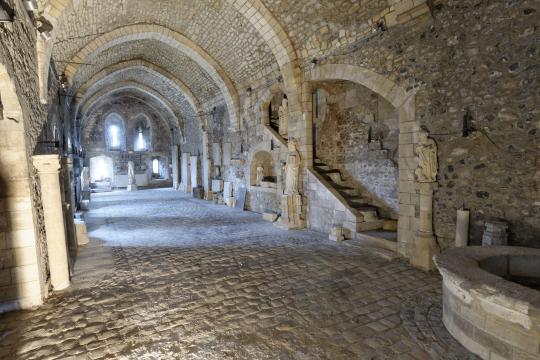 Grande salle basse voûtée en arc brisés, escalier menant à l'ancien réfectoire et puits à droite.